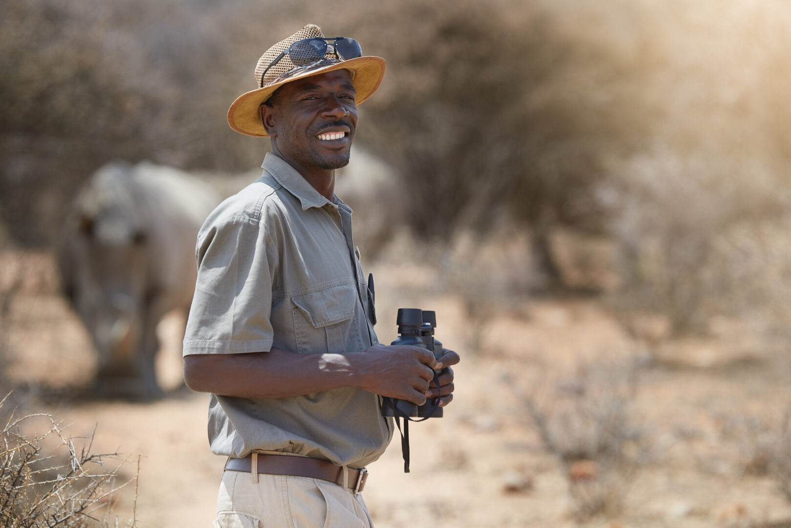 Wildlife Vacations: Portrait, safari and wildlife with a man ranger outdoor in a game park for nature conservation. Animals, binoculars and blurred background with an african male person on patrol in the wilderness