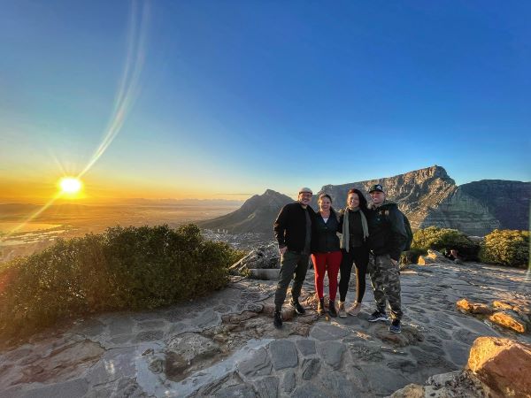 Four friends pose for a photo in front of South Africa's Table Mountain at sunset.
