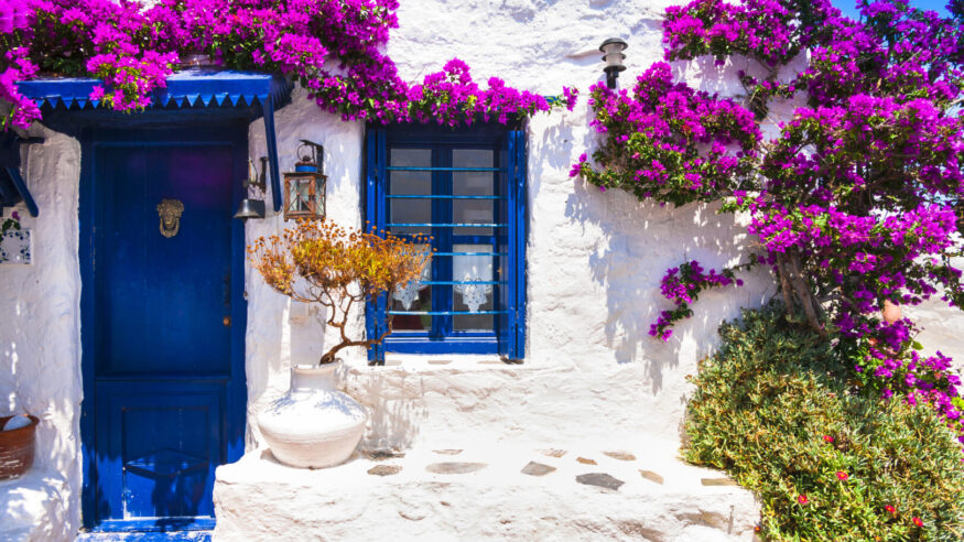 Charming typical floral streets of Greek islands with whitewashed houses and blue doors