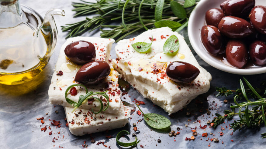 Feta cheese with olives and green herbs on gray marble background